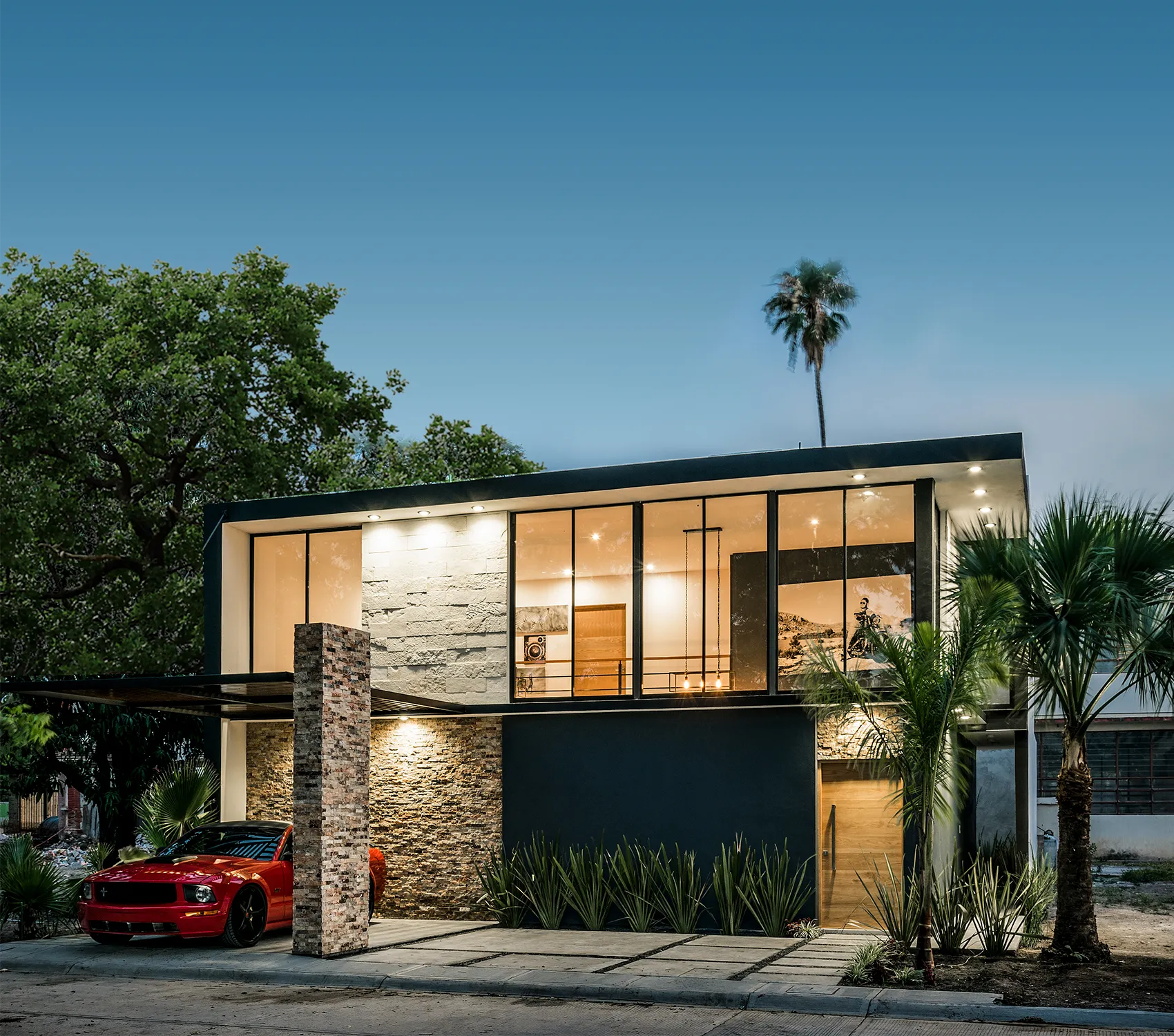 fachada residencial moderna iluminada al anochecer, destacando la transparencia del cristal y la piedra decorativa.