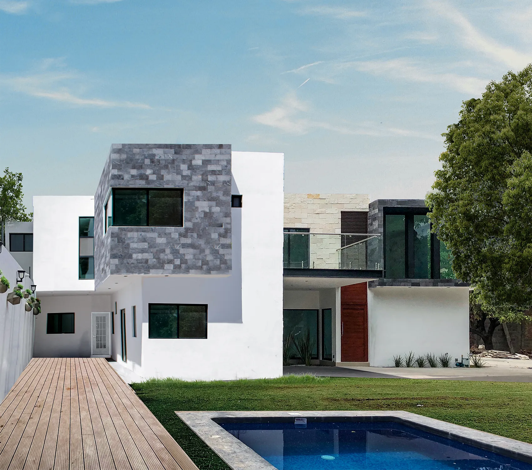 Fachada posterior de residencia moderna con alberca: vista del jardín mostrando un camino de deck de madera, piscina privada y volúmenes arquitectónicos con revestimiento de piedra gris.